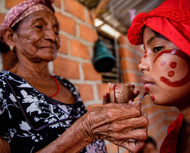 Wayuu Frau bemalt auf tradionelle Art ihre Enkelin in Kolumbien © IMAGO / SOPA Images
